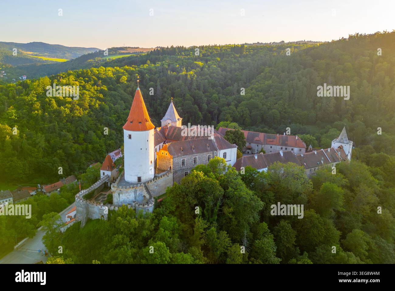 Il Castello di Krivoklat è splendidamente illuminato durante il tramonto, circondato da verdi foreste. Questa struttura medievale della Boemia centrale mostra le sue imponenti torri e il suo significato storico. Foto Stock