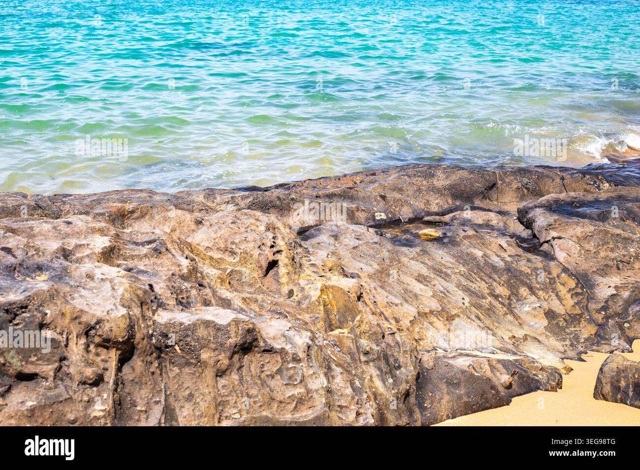 Il mare turchese lambisce dolcemente su una costa rocciosa con sabbia dorata a Khao Lak, Thailandia. spiaggia tropicale, vista oceano, paesaggio costiero. Foto Stock