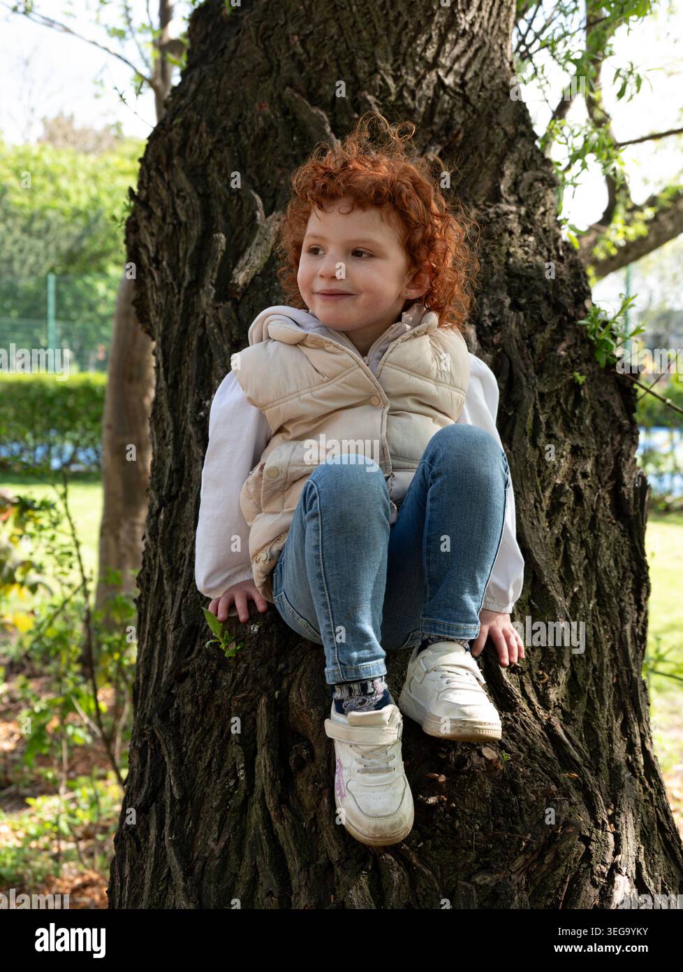 bambino dalla testa rossa seduto sul tronco di un albero. Foto Stock