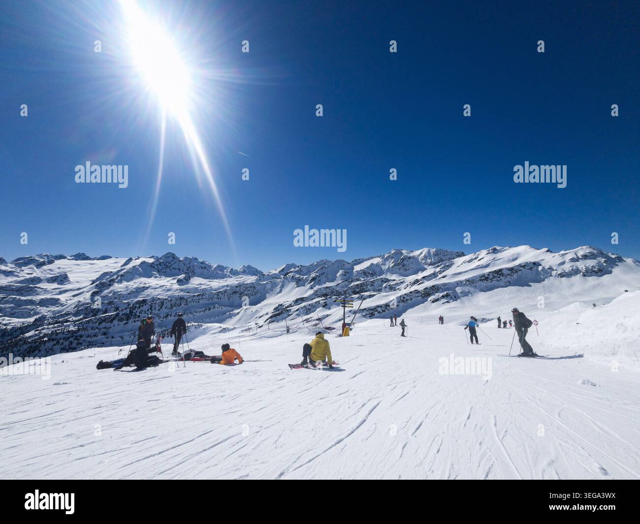 Sciatori e snowboarder che riposano e cavalcano su un'ampia pista innevata sotto un sole brillante e scintillante con una spettacolare luce ottica a la Thuile Ski Re - Immagine stock catturata con smartphone