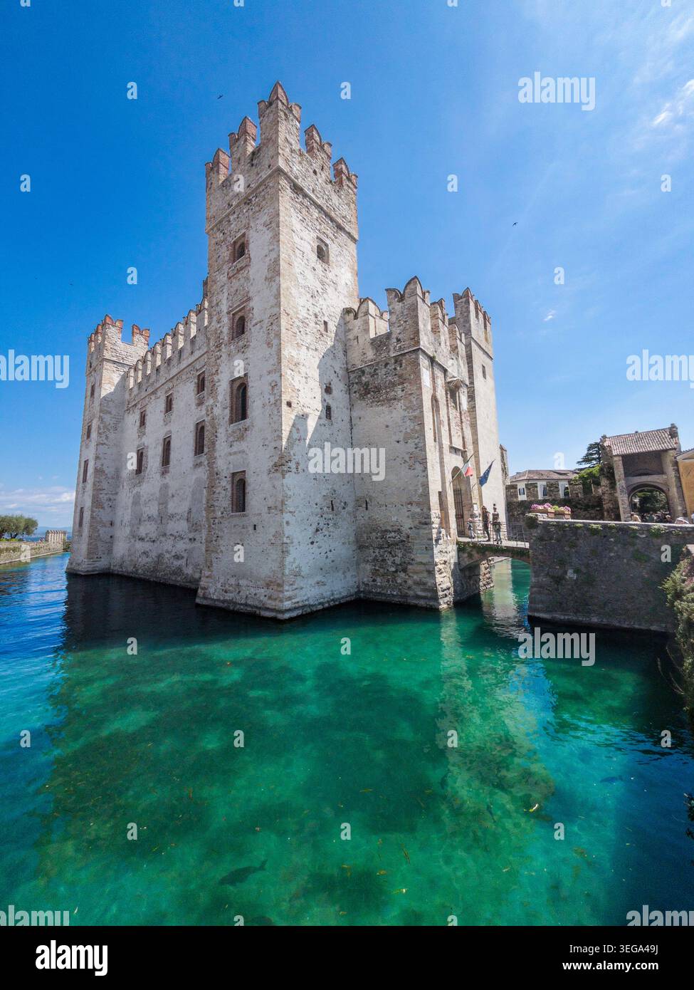 Lo storico Castello Scaligero di Sirmione sorge direttamente dalle acque cristalline e turchesi del Lago di Garda in una giornata luminosa e soleggiata. - Immagine stock catturata con smartphone