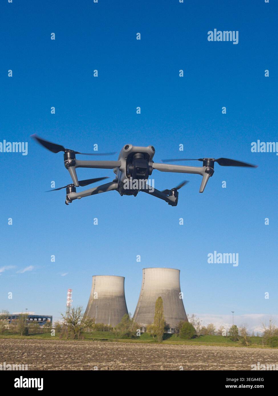 drone che sorvola a mezz'aria contro un cielo blu limpido, con due torri di raffreddamento industriali di una centrale elettrica visibili sullo sfondo. - Immagine stock catturata con smartphone