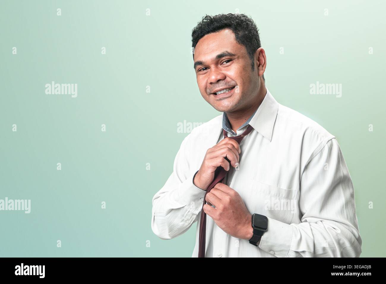 Un uomo indonesiano professionista in abito nero incrocia le braccia presentando uno spazio bianco con una mano aperta su uno sfondo verde. Foto Stock
