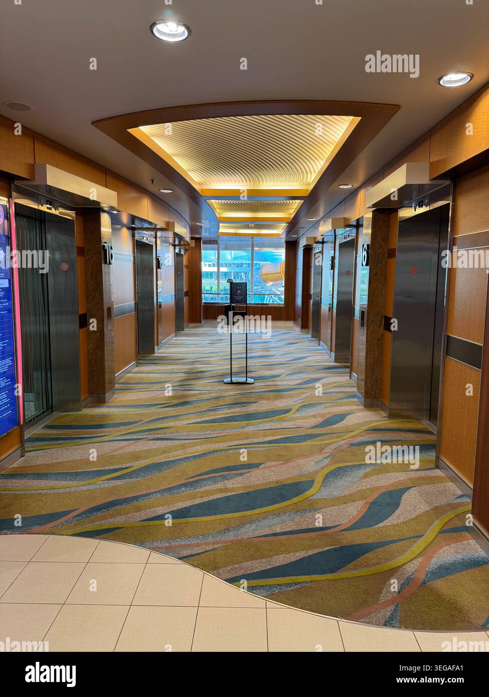 Un elegante corridoio della lobby con ascensore con tappeti a onde e pannelli di legno scuro all'interno di una nave da crociera. Foto Stock