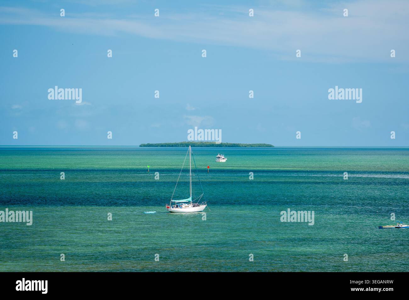 Una barca a vela bianca ancorata nelle acque cristalline dell'oceano turchese vicino a una lontana isola verde al largo della costa di Key West nelle Florida Keys. Foto Stock