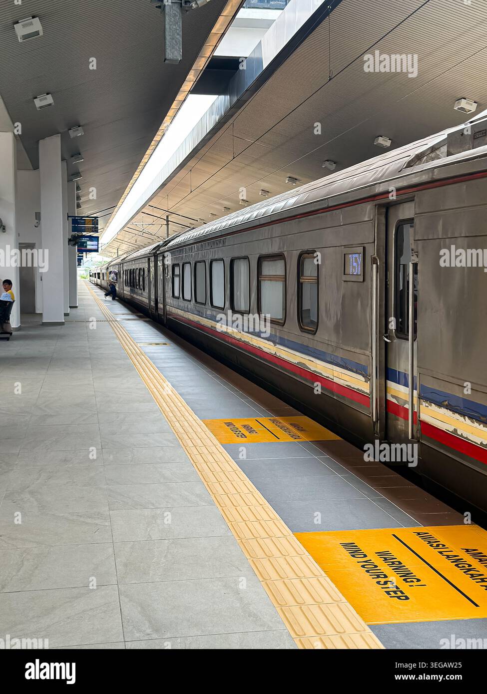Treno passeggeri Silver sulla piattaforma della stazione pulita con segnali di sicurezza bilingue e pavimentazione tattile. Foto Stock
