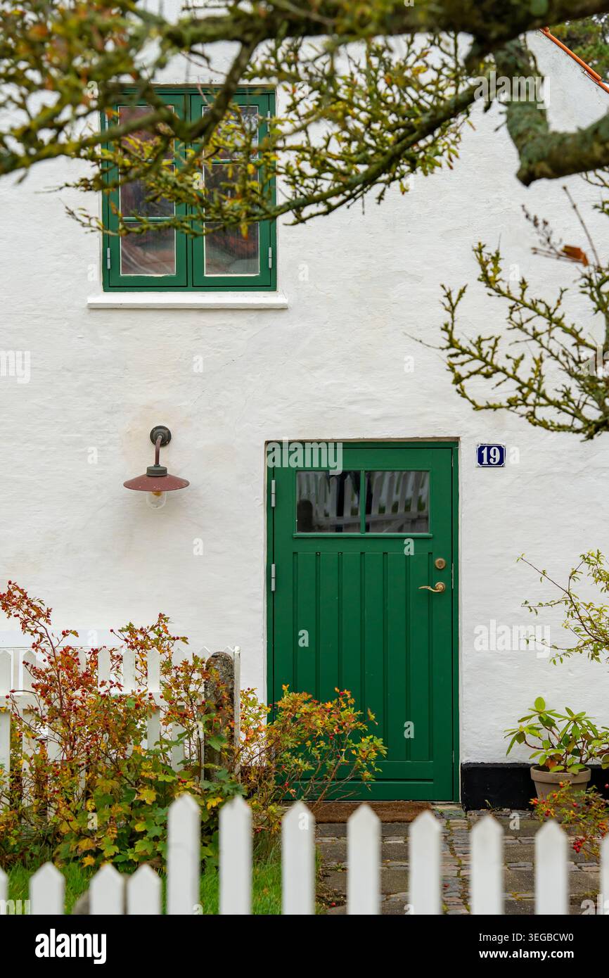 Un tradizionale cottage europeo a Skagen, Danimarca. La casa ha pareti dipinte di bianco e una porta di legno verde scuro e telai delle finestre Foto Stock