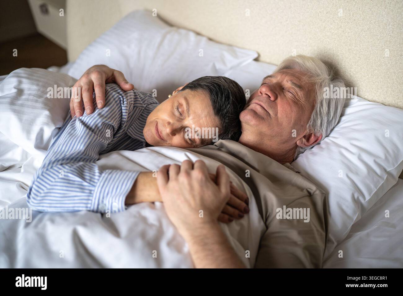 Marito e moglie di una coppia senior positiva che dormono a letto insieme e si abbracciano dolcemente con tenerezza. Foto Stock