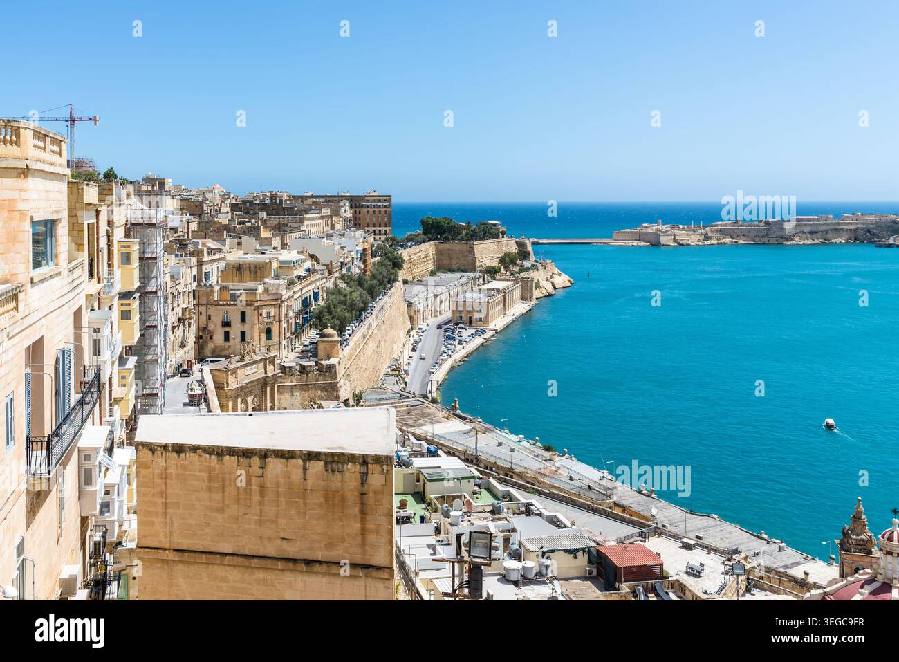 Vista panoramica costiera di la Valletta con edifici storici in pietra calcarea, mura fortificate e acque turchesi del Mediterraneo sotto un cielo azzurro Foto Stock