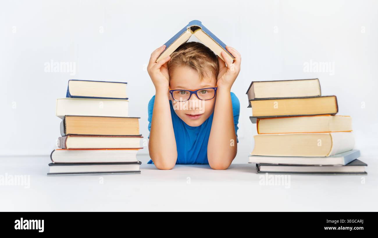 un ragazzo sorridente con molti libri tiene il libro come un tetto sopra la sua testa. Concetto di sicurezza nell'apprendimento. Foto Stock