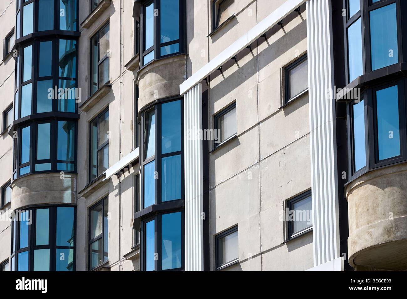 La facciata di un moderno edificio residenziale presenta pareti in cemento grigio con finestre in vetro blu. L'architettura geometrica mostra l'esterno del blocco di appartamenti urbani Foto Stock