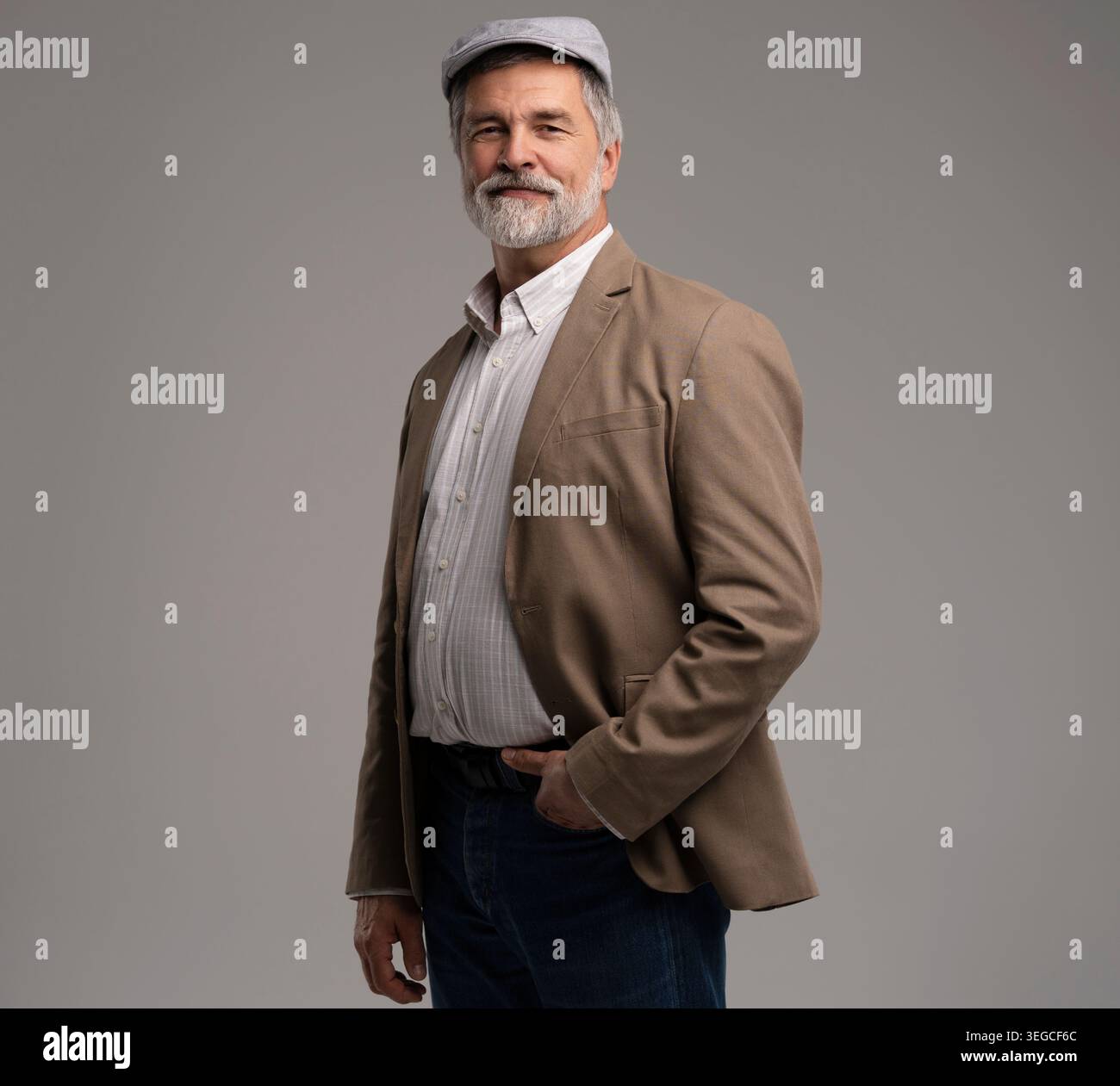 Elegante e serio uomo dai capelli grigi in tuta e cappuccio piatto isolato su sfondo grigio Foto Stock
