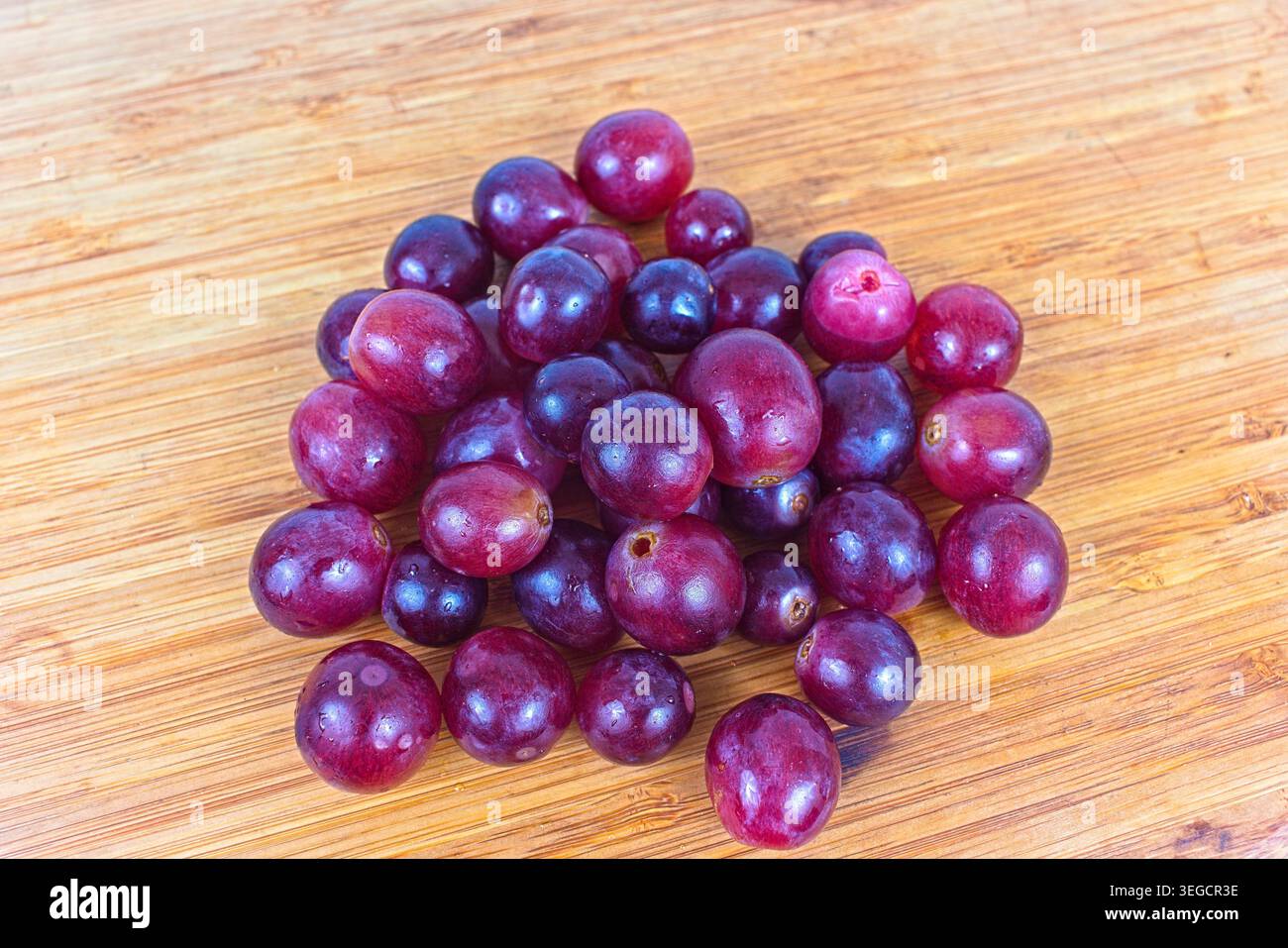 Un vivace gruppo di uve rosse mature poggia su una superficie in legno testurizzato, che mostra la loro bellezza naturale e la loro freschezza. Foto Stock