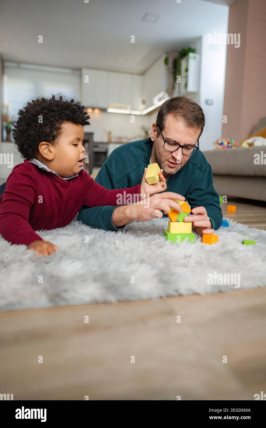 Padre e figlio costruiscono blocchi insieme che giocano per terra Foto Stock