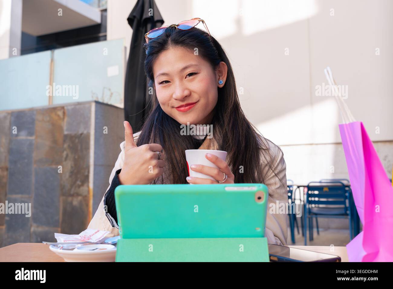 Felice donna asiatica che si fa dare i pollici in un bar all'aperto con un tablet Foto Stock