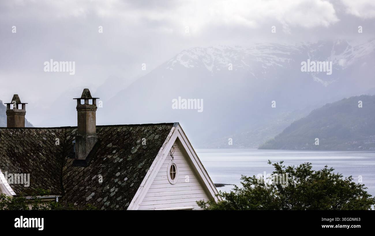 Atmosfera da fiordo nebbioso, vecchio tetto con vista sul fiordo Hardangerfjord coperto dalla pioggia e sulle montagne a strati a Lofthus, Norvegia, che riflettono il mutare del clima nordico Foto Stock