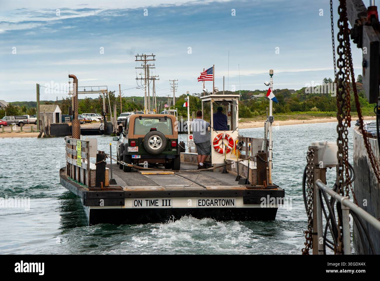 Vista del traghetto Chappaquiddick sul Time III che trasporta un veicolo sull'acqua con membri dell'equipaggio e una bandiera americana di Edgartown, Massachusetts, Unit Foto Stock