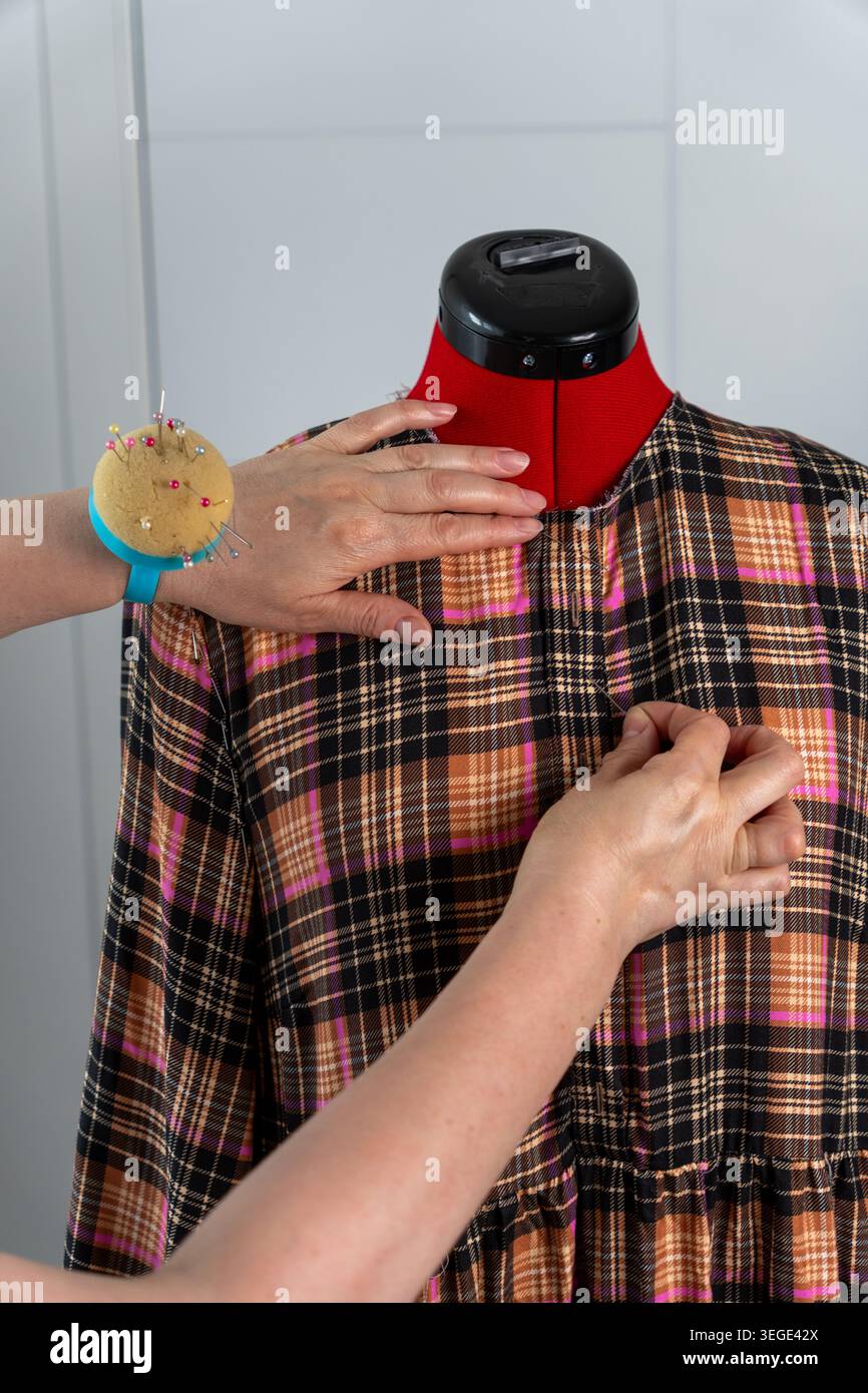 Primo piano verticale di una donna che regola e fissa il tessuto su un manichino sartoriale durante il montaggio e il processo di creazione della sartoria. Un lavoro sartoriale dettagliato con texti Foto Stock