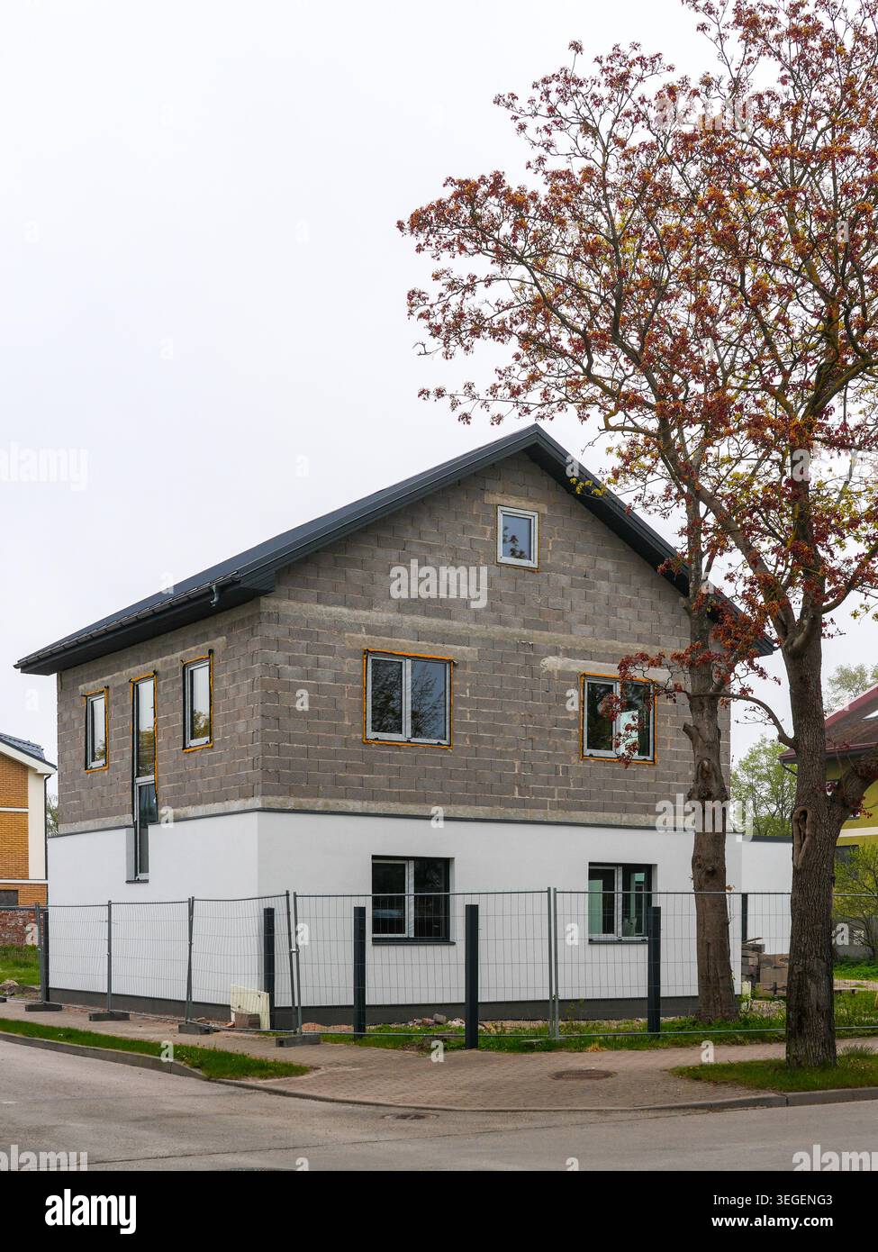 Casa moderna parzialmente rifinita con facciata in blocchi di cemento e albero autunnale nel quartiere urbano di Liepaja, Lettonia Foto Stock