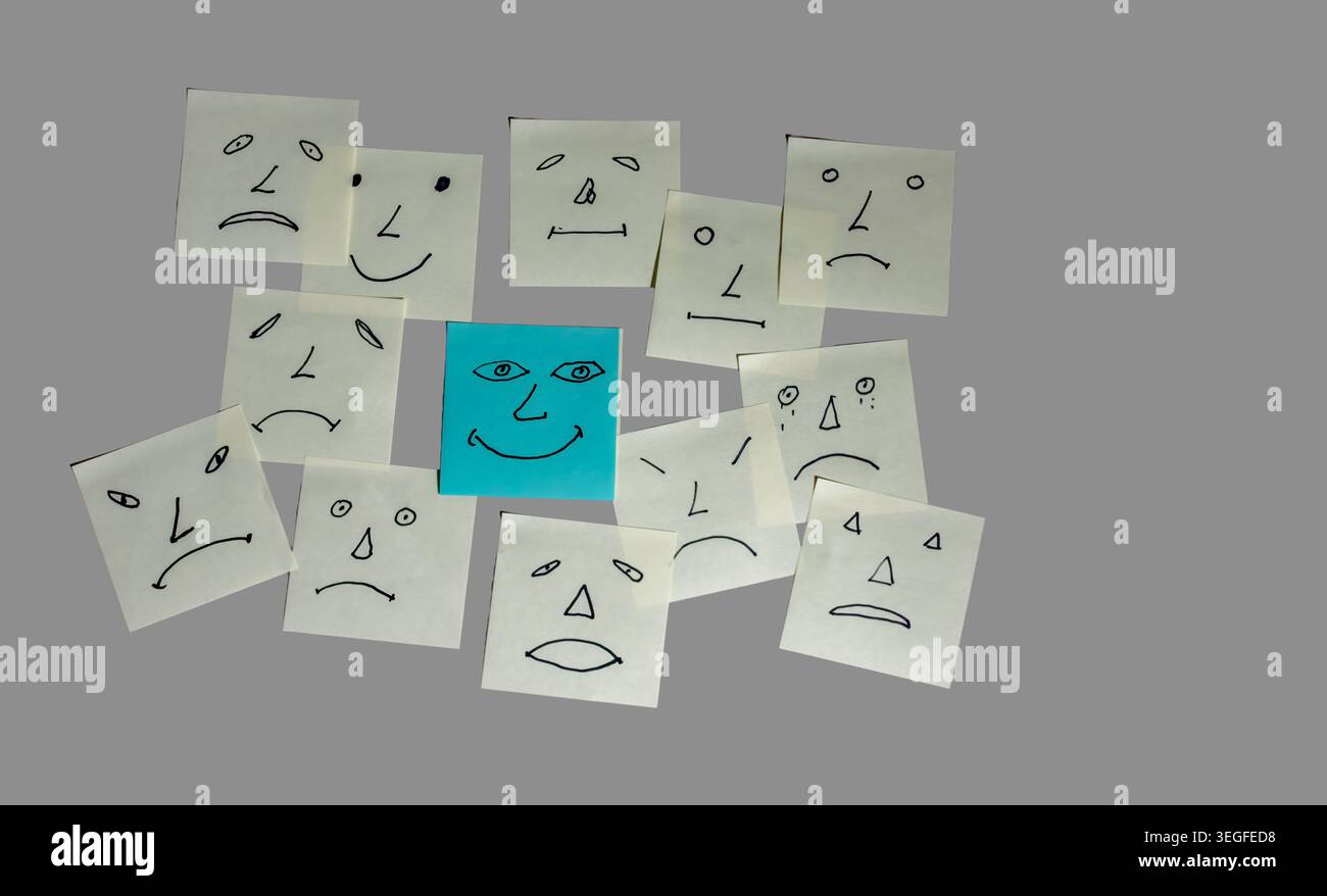 Le note con varie facce sono disposte intorno a una faccia felice centrale. Ogni faccia ha un'espressione diversa. Le note cartacee sono posizionate su uno sfondo grigio che mostra un layout semplice. Foto Stock