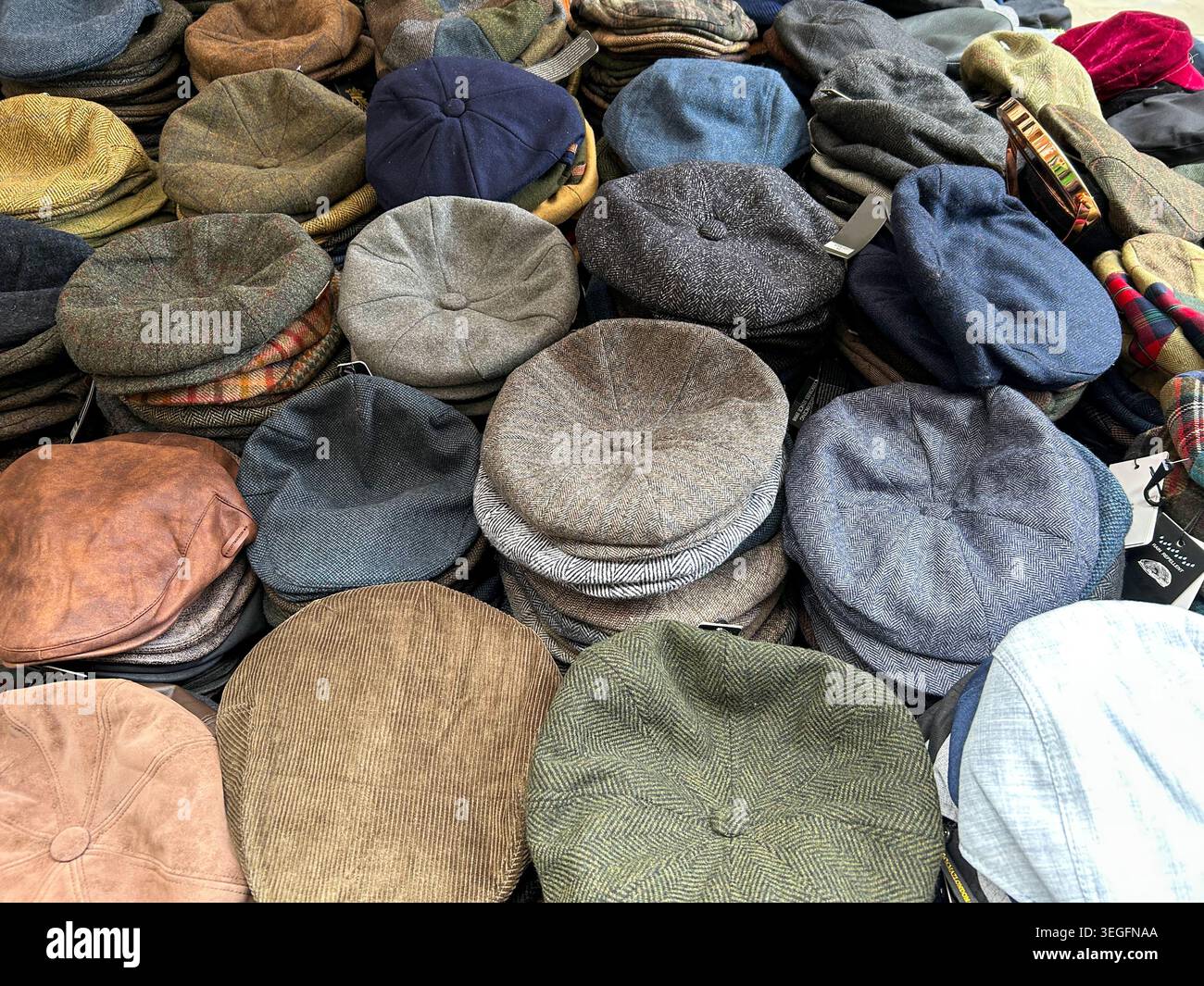 Vista dall'alto verso il basso di pile di classici cappelli piatti in tweed, lana, velluto a coste e pelle e cappelli newsboy in diversi colori e motivi in un mercato di abbigliamento Foto Stock