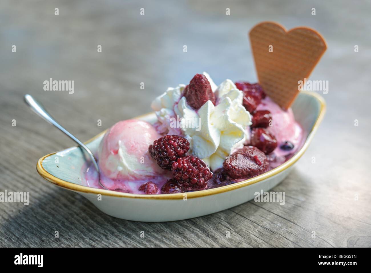 Sundae, palline di gelato con composta di frutta e panna montata in una lunga ciotola su un tavolo di legno, dessert estivo, spazio per copiare, focalizzazione selezionata, stretto Foto Stock