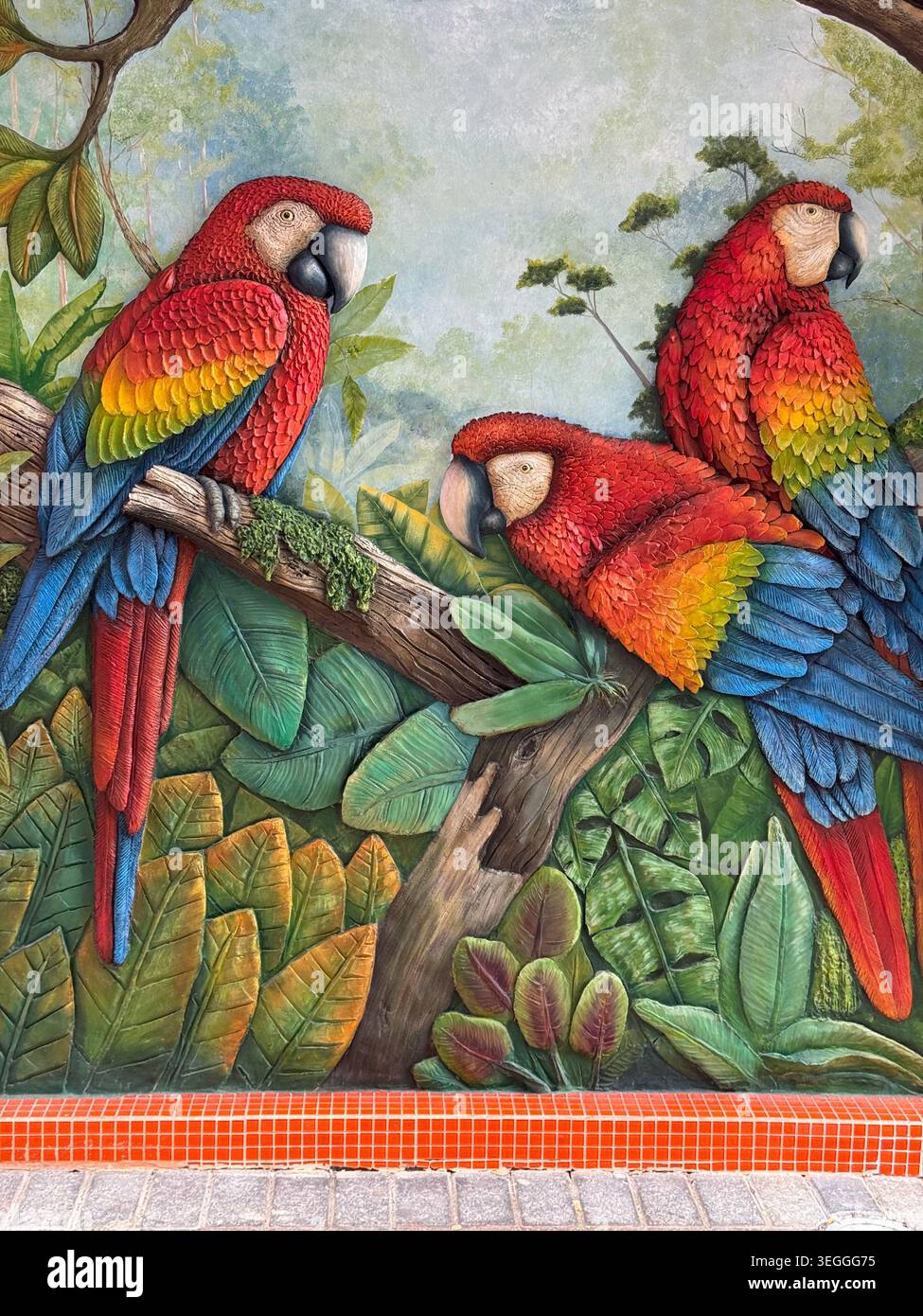 Un vivace dipinto colorato che raffigura tre pappagalli rosso scarlatto arroccati su rami di alberi della giungla tropicale. - Immagine stock catturata con smartphone
