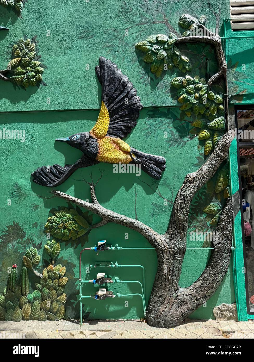 Un bellissimo e vibrante dipinto su una parete gialla raffigurante un uccello tropicale venezuelano seduto su un cactus fiorito. - Immagine stock catturata con smartphone