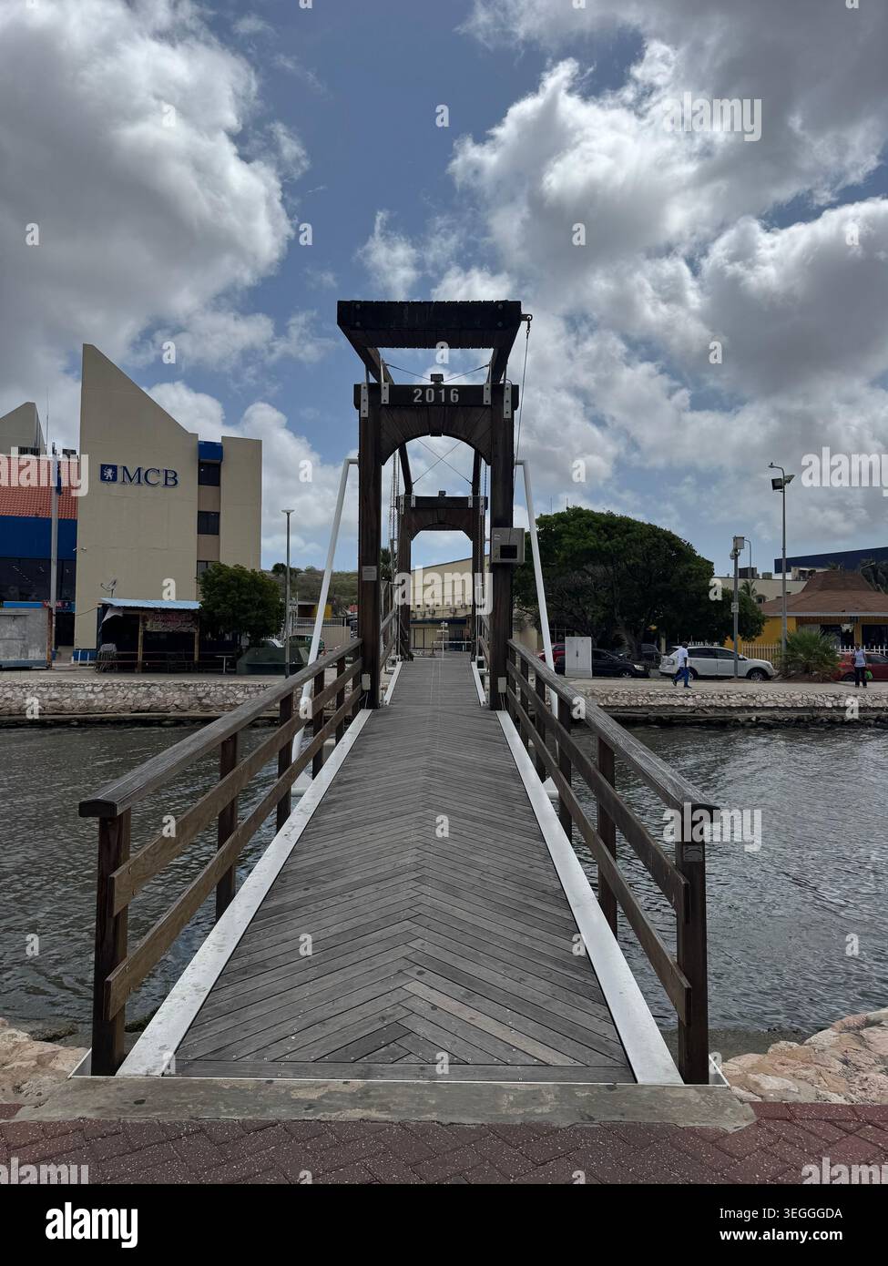 Vista prospettica di uno stretto ponte pedonale in legno che conduce sul canale d'acqua verso la città di Willemstad, Curacao. - Immagine stock catturata con smartphone