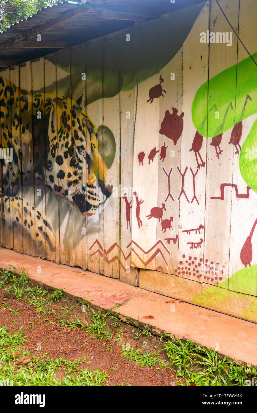Raudal del Guayabero, Guaviare, Colombia - 1° maggio 2026 - murale Jaguar accanto a pittogrammi rossi che illustrano antiche espressioni culturali. Foto Stock