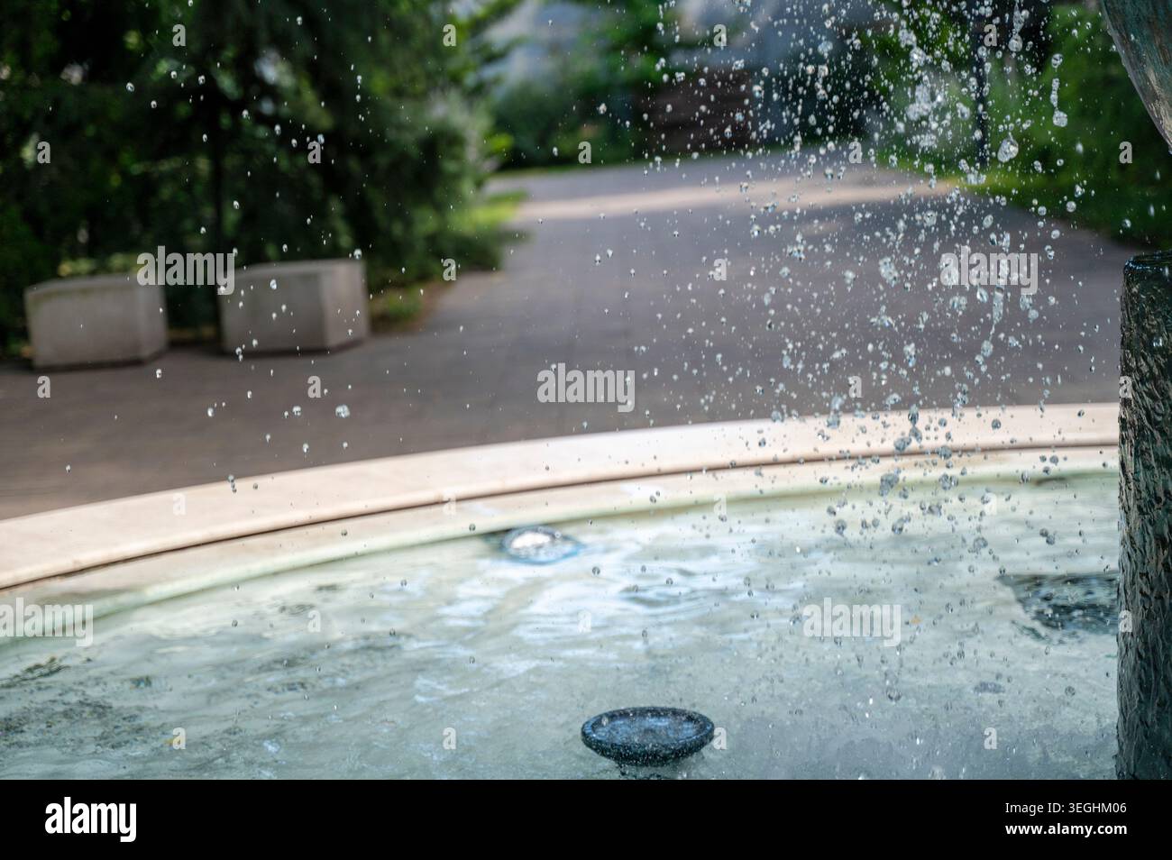 Fontana decorativa con gocce d'acqua volanti in un giardino pubblico soleggiato. Liquido trasparente. Concetto di arte idraulica, design di parchi ricreativi e strutture stagionali Foto Stock