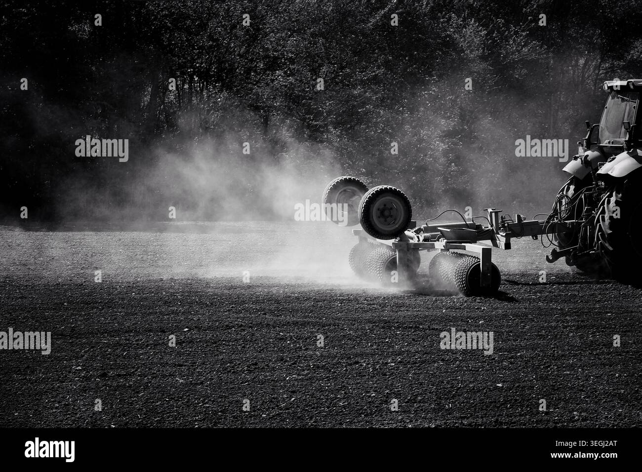 Fotografia in bianco e nero di un trattore con un rimorchio che attraversa un campo, che solleva la polvere Foto Stock