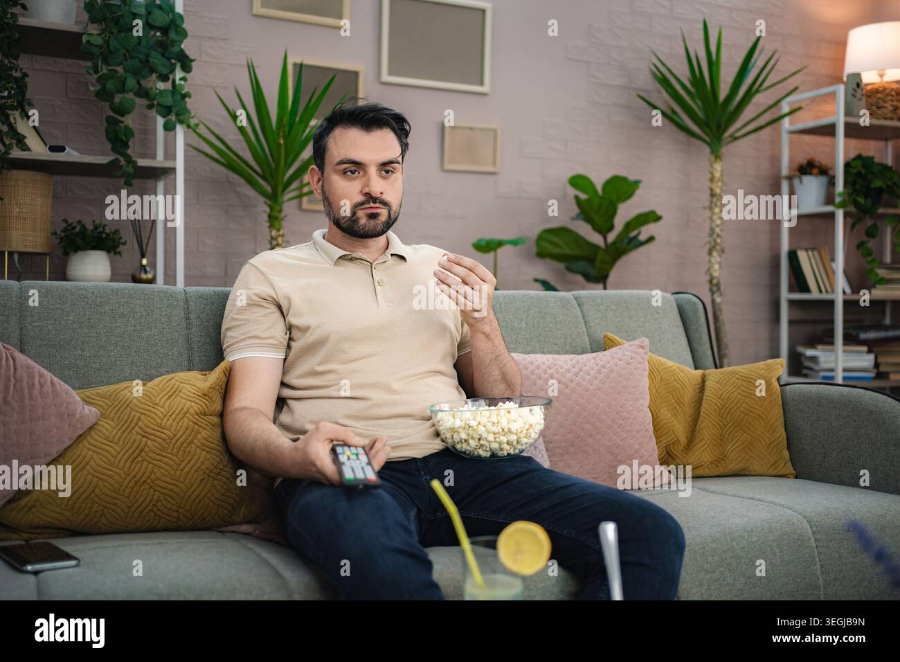 Giovane che guarda la televisione mentre mangia popcorn sul divano Foto Stock