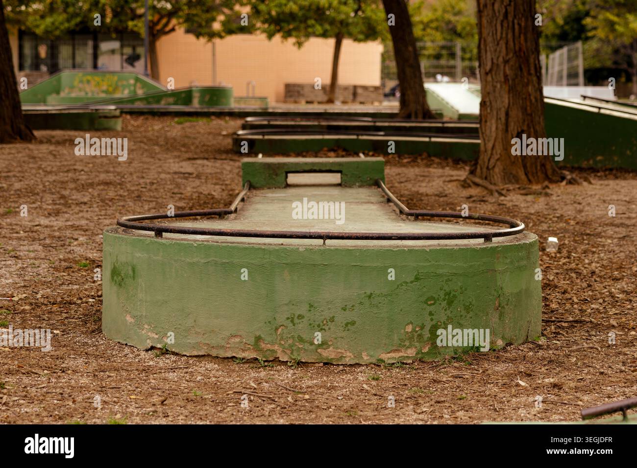 Vecchio campo da golf in miniatura verde in un parco, circondato da terreni sterrati e alberi, con bassa profondità di campo e toni caldi, che suggeriscono attività ricreative abbandonate Foto Stock