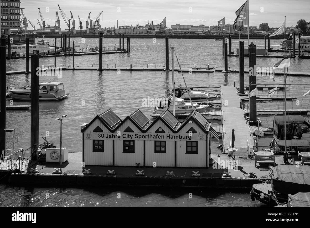 Vista in bianco e nero del porticciolo di Sporthafen, con barche, moli galleggianti, edifici portuali e gru portuali industriali sullo sfondo, cap Foto Stock