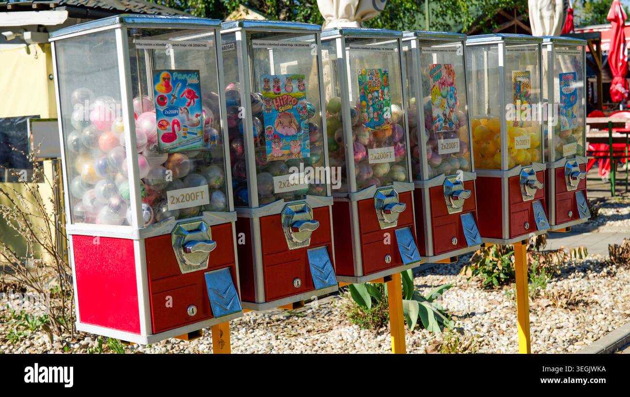 fila di distributori automatici di giocattoli e gommoni con capsule colorate, attrazione rétro per bambini per aree giochi all'aperto e zone di intrattenimento per famiglie Foto Stock