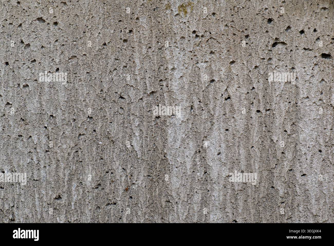 Primo piano di una parete in cemento grigio ruvido con dettagli porosi della superficie, sottili segni verticali e imperfezioni naturali Foto Stock