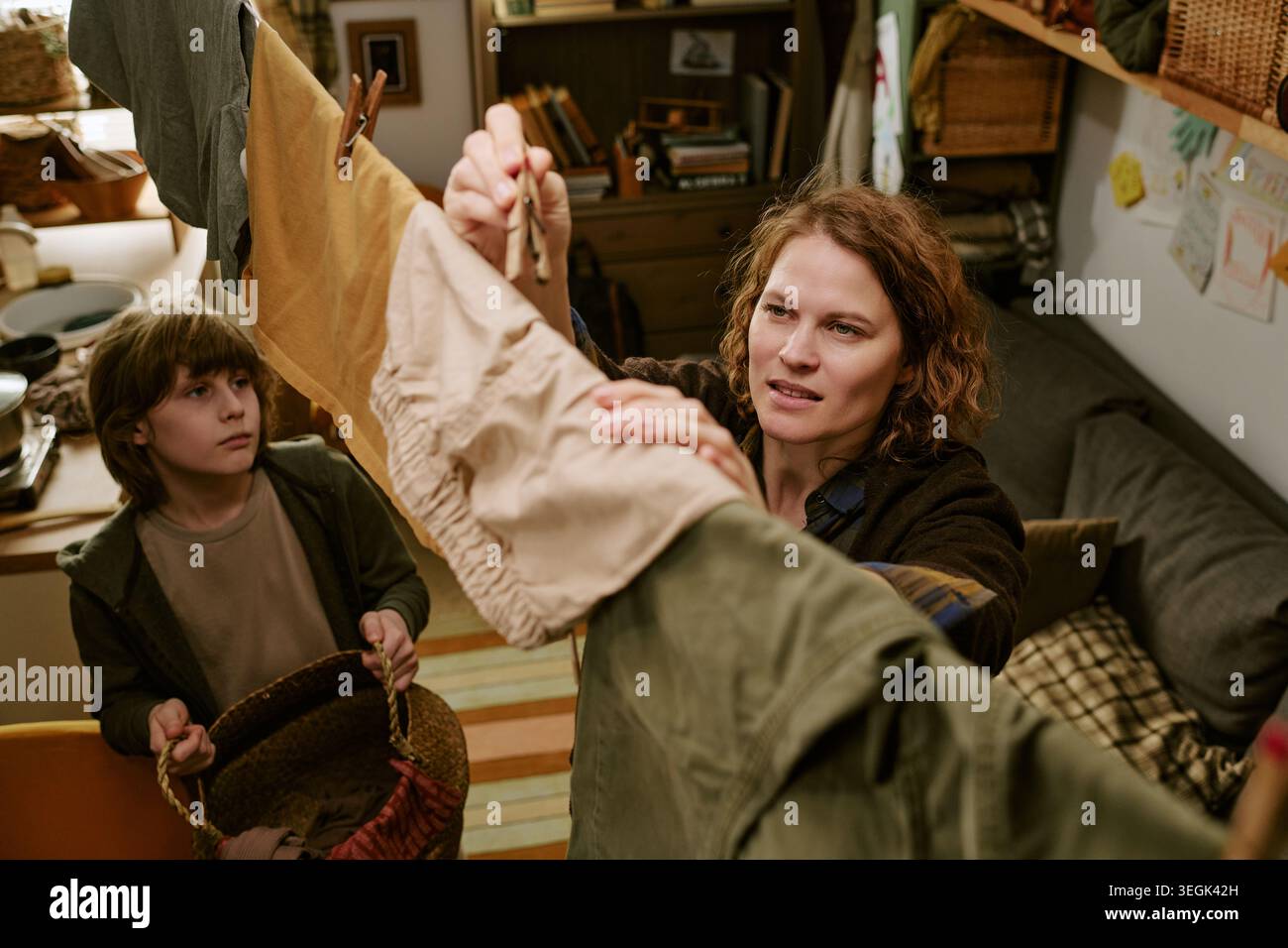 Donna adulta che appende il bucato a casa con bambino che aiuta nelle faccende domestiche Foto Stock