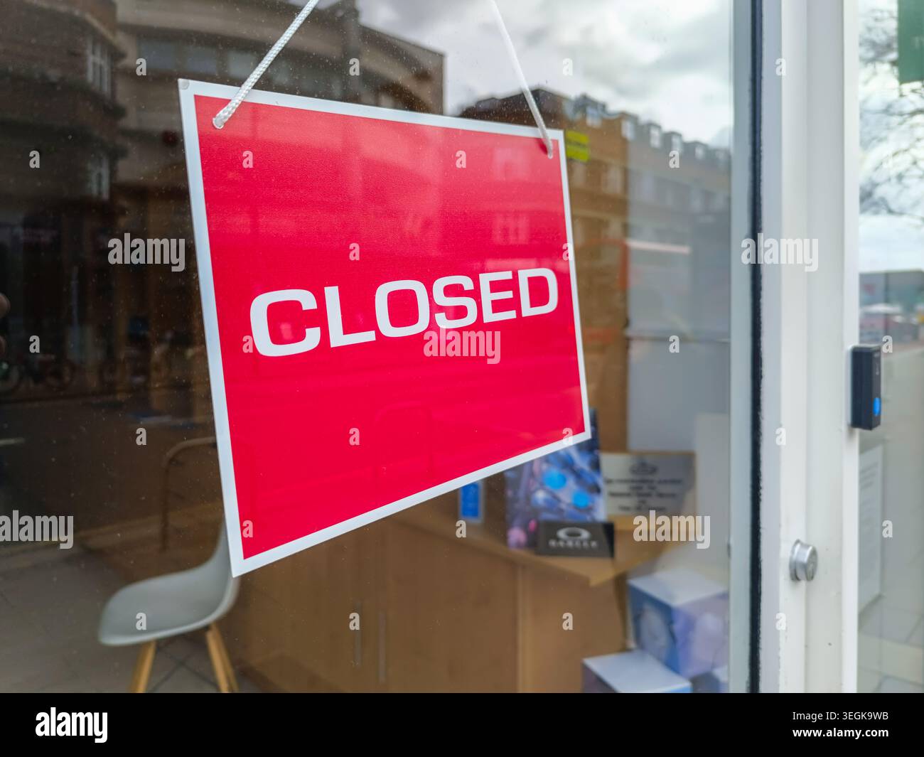 Cartello rosso chiuso appeso su una porta di vetro di un negozio locale Foto Stock