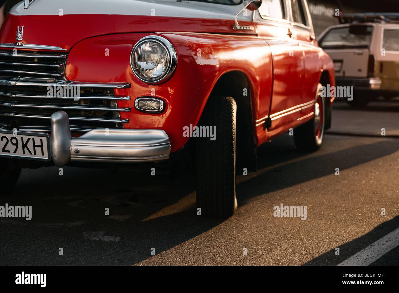 Vintage GAZ-20 Pobeda sotto i raggi del sole che tramonta. Auto sovietica bicolore rossa e bianca degli anni '1940 con griglia cromata e faro rotondo parcheggiato con ruota girata. Foto Stock