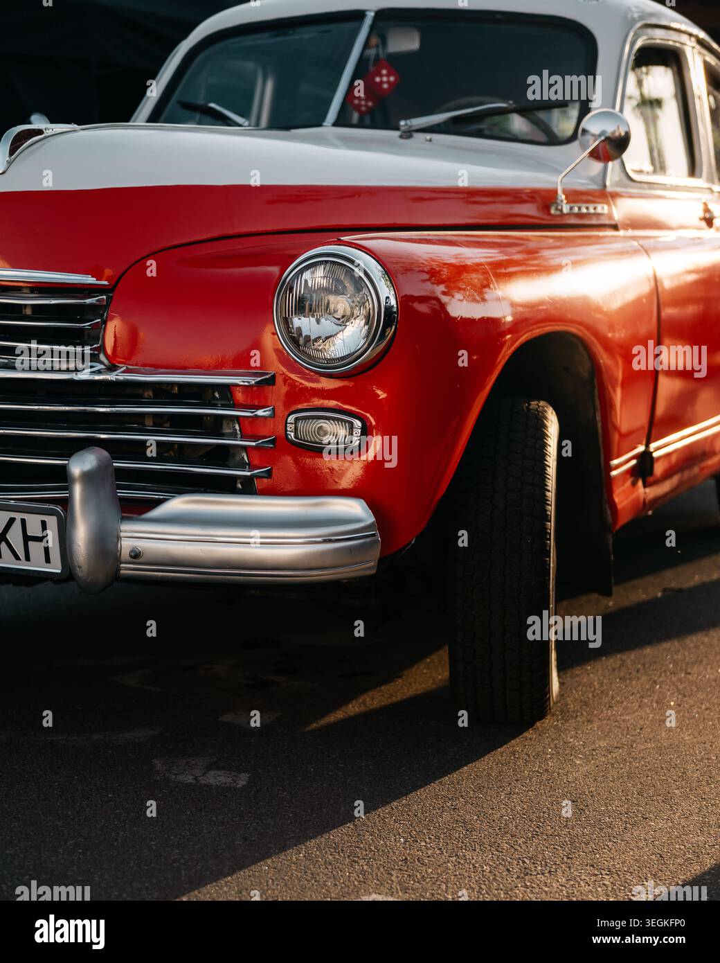 Primo piano di Pobeda vintage GAZ-20 al tramonto. Auto sovietica bicolore rossa e bianca degli anni '1940 con griglia cromata e faro rotondo parcheggiato con ruota girata. Foto Stock