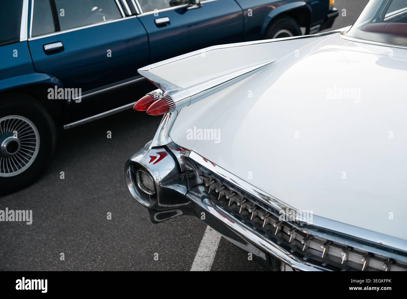 Auto americana bianca degli anni '1950 parcheggiata vicino alla berlina blu degli anni '1980. Vista ravvicinata dell'angolo posteriore dello yacht jet age Land con grande pinna di coda e paraurti cromato. Foto Stock