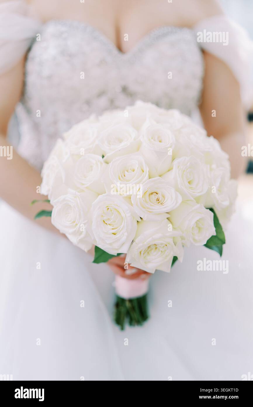 Raffinata posa a mano che sfoggia un lussureggiante bouquet di rose bianche con un morbido sfondo luminoso Foto Stock