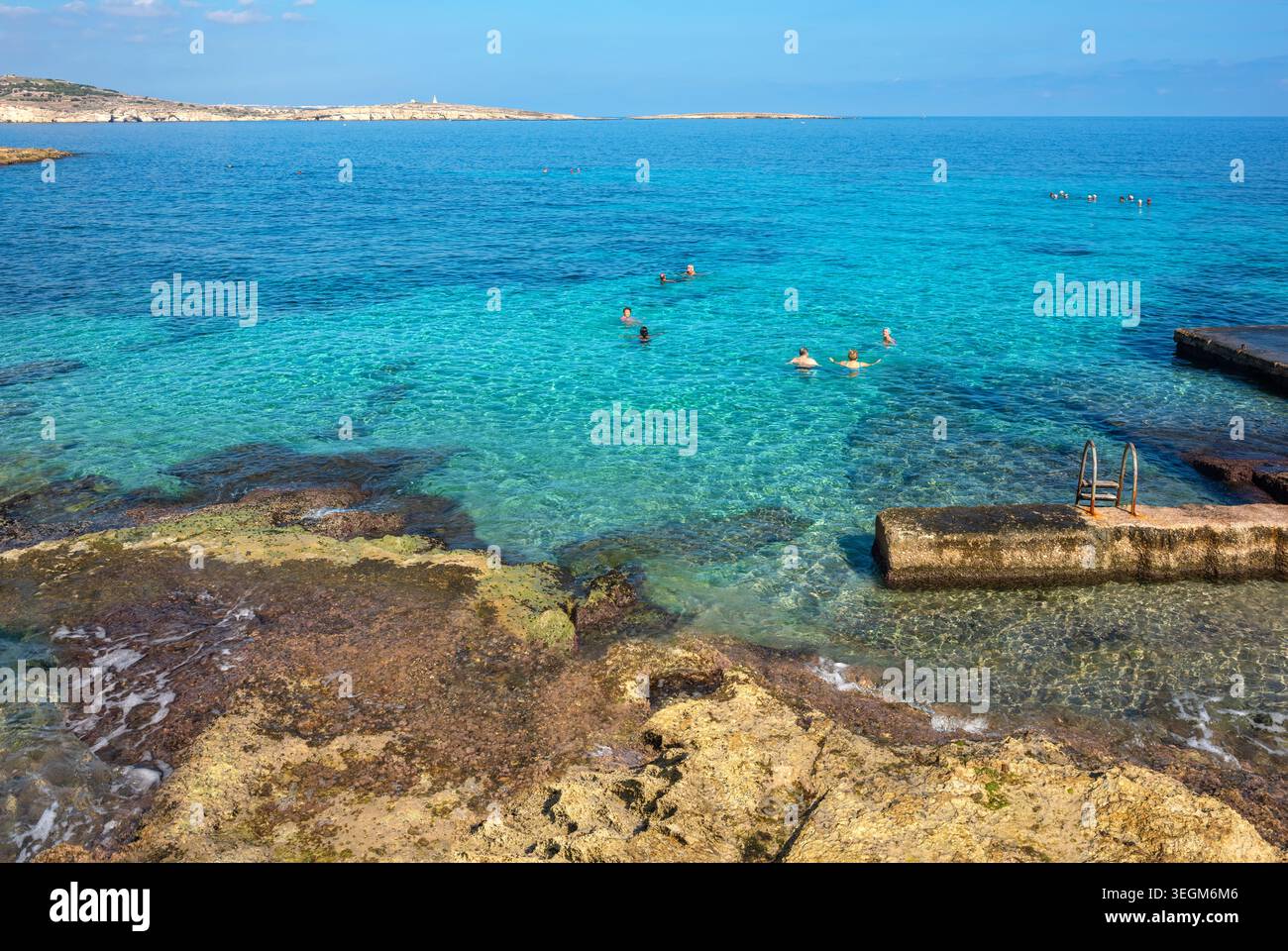 Le persone che si bagnano godendosi l'acqua di mare turchese presso la spiaggia rocciosa naturale sul mare della baia di San Giuliano. Malta Foto Stock
