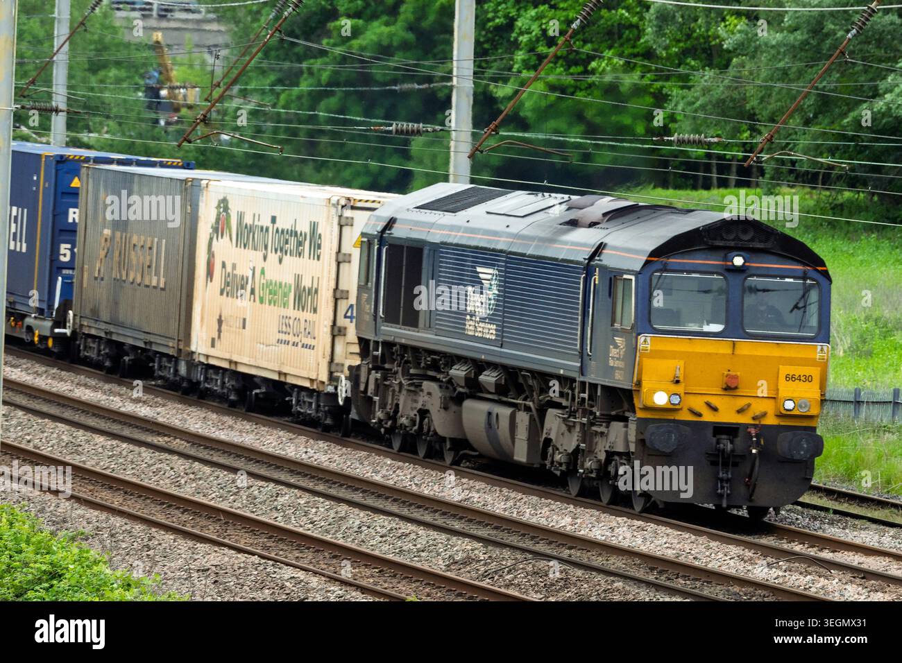 Una potente locomotiva diesel classe 66 trasporta un lungo treno di container colorati attraverso Winwick, mostrando la vivace attività della ferrovia tran Foto Stock