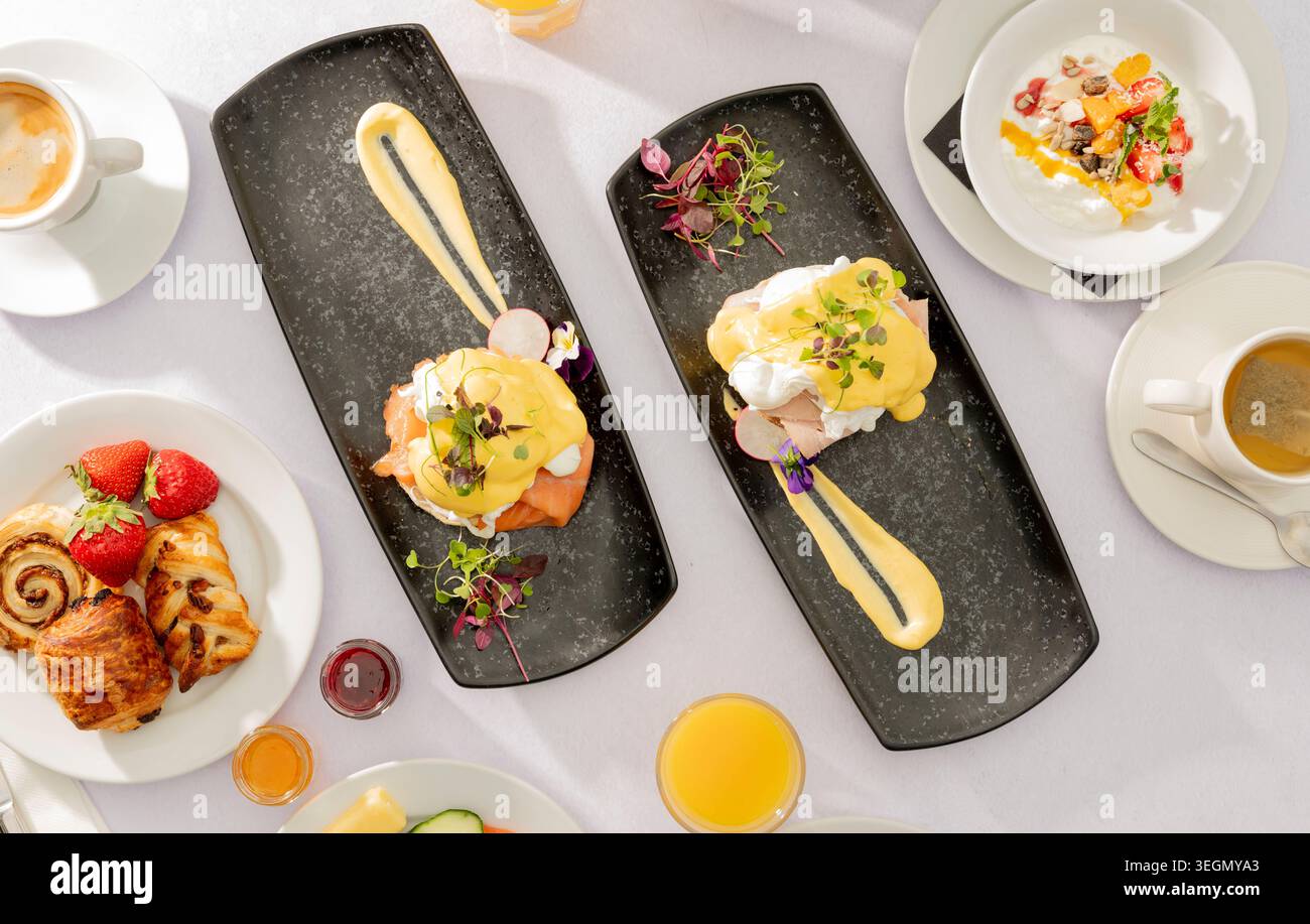 Delizioso brunch con uova Benedict, pasticcini e bevande rinfrescanti per una giornata di sole Foto Stock