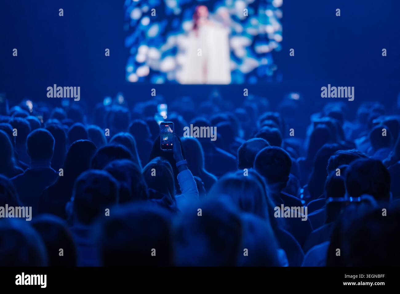 Il pubblico cattura concerti dal vivo su smartphone, illuminazione del palcoscenico blu, esibizioni di folla affollate, condivisione sociale e atmosfera di eventi. Foto Stock