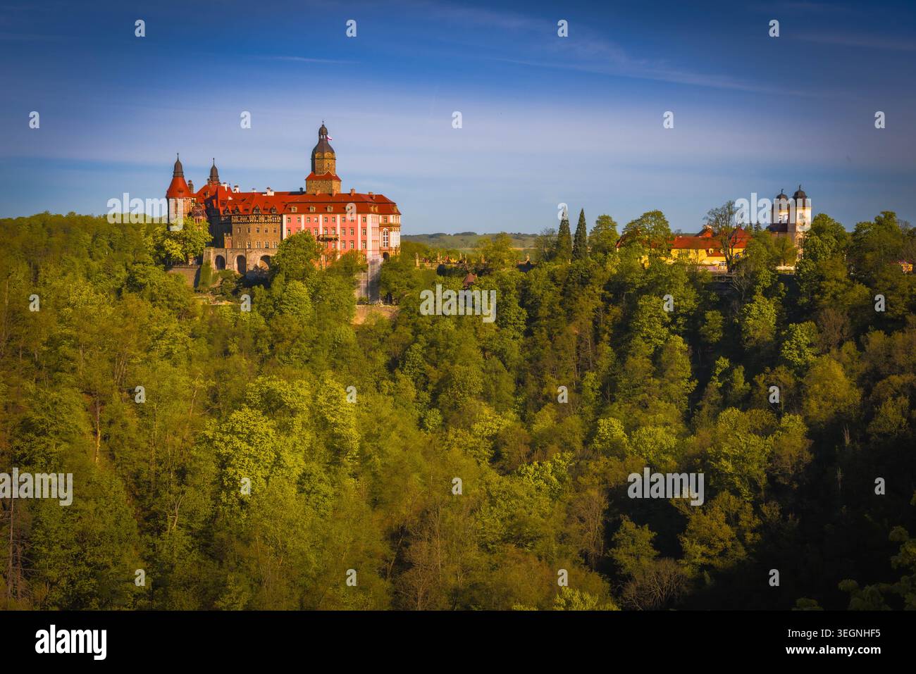 Panorama primaverile del castello di Ksiaz a Walbrzych, Polonia, che si innalza sopra una lussureggiante foresta verde sotto il cielo blu, visto da una collina lontana. In primavera brillante. Foto Stock
