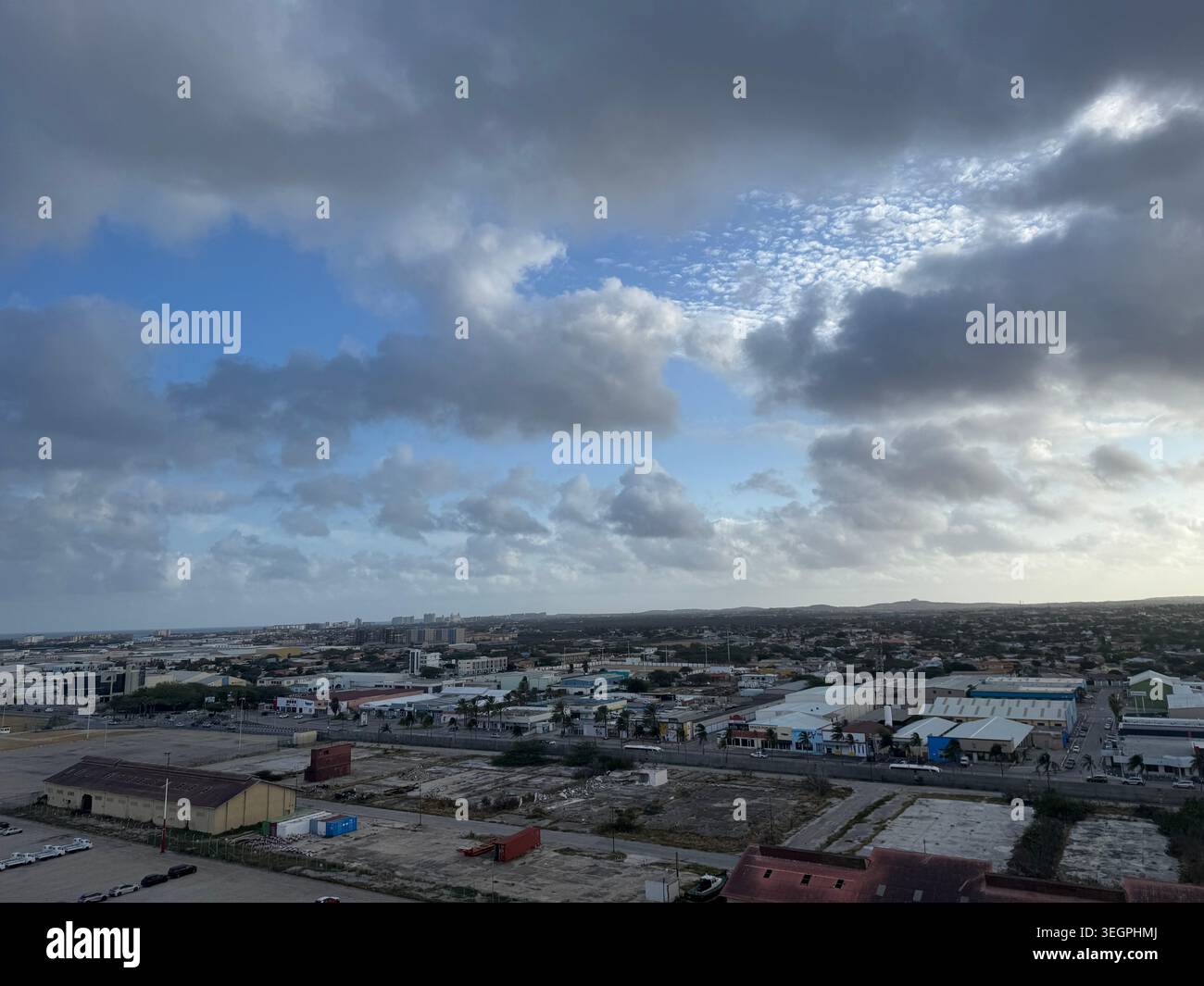 Vista elevata e grandangolare di una città costiera e dell'area portuale industriale sotto un cielo nuvoloso e pesante. AL MATTINO AD ARUBA, mentre navighi - Immagine stock catturata con smartphone