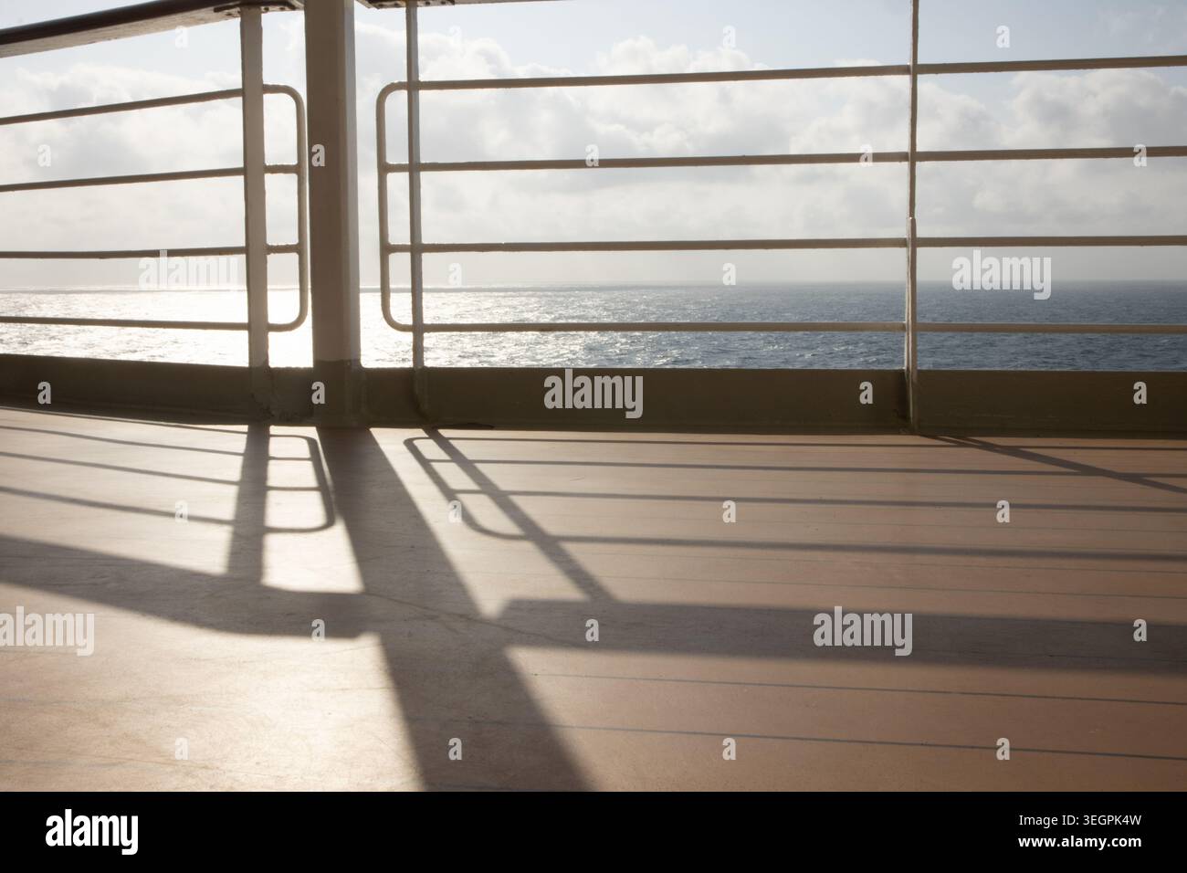 Tranquille vedute dell'oceano da una nave da crociera di lusso, sole basso che risplende sul mare, gettando lunghe ombre sul ponte della passeggiata Foto Stock